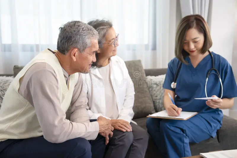 Asian female nurse talking with an older couple at home